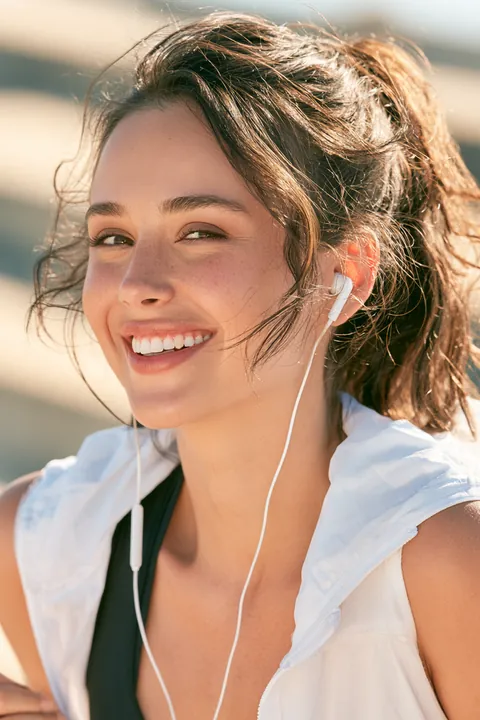 Young woman in her twenties wearing wireless headphones, pausing mid-run to catch her breath and smile, a moment of calm before reading the Hidden Meadow Lending blog