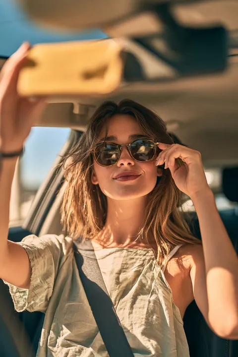Over-the-shoulder view of a woman in her thirties adjusting the rearview mirror of her compact car before a drive, a reminder that Hidden Meadow Lending helps with everyday costs