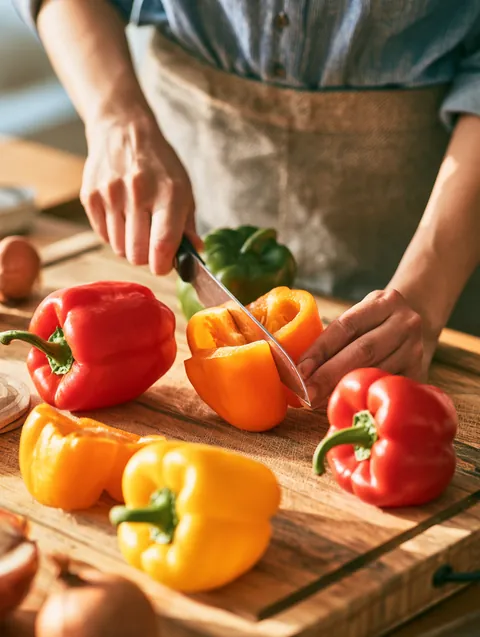 Woman slicing fresh bell peppers on a butcher-block counter while planning her household budget with Hidden Meadow Lending