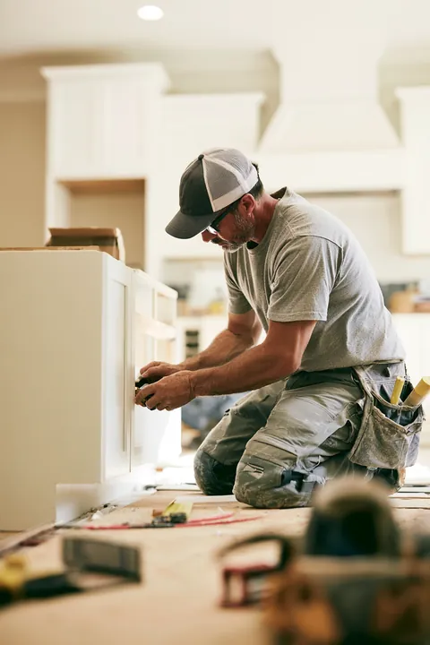 Over-the-shoulder view of a handyman measuring a kitchen cabinet with a tape measure, an early step in a Hidden Meadow Lending repair budget