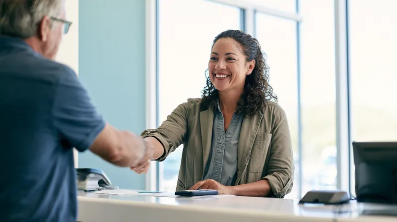 Patient in his 50s shaking hands with a clinic billing coordinator at a bright reception desk after agreeing on a payment plan