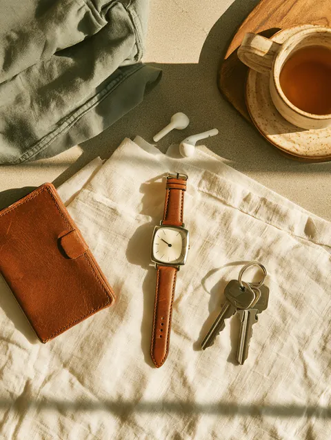 Top-down flat lay of a smartwatch, earbuds, a wallet and keys on crisp linen, everyday costs a Hidden Meadow Lending reader might budget for