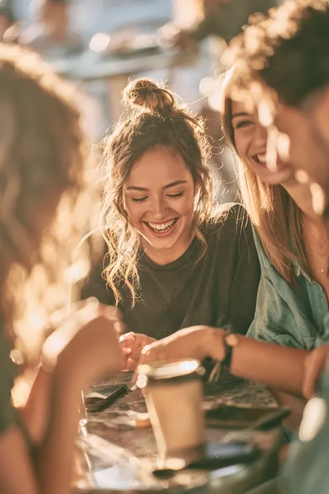 Group of friends in their 20s laughing together around a cafe table, the kind of budget a Hidden Meadow Lending guide helps protect