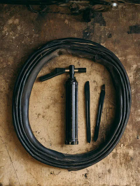 Top-down view of a bicycle inner tube, mini pump and tire levers laid out on a garage workbench