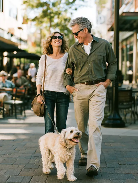 Couple in their 50s walking their dog through a lively downtown neighborhood, the kind of everyday life a Hidden Meadow Lending guide aims to protect